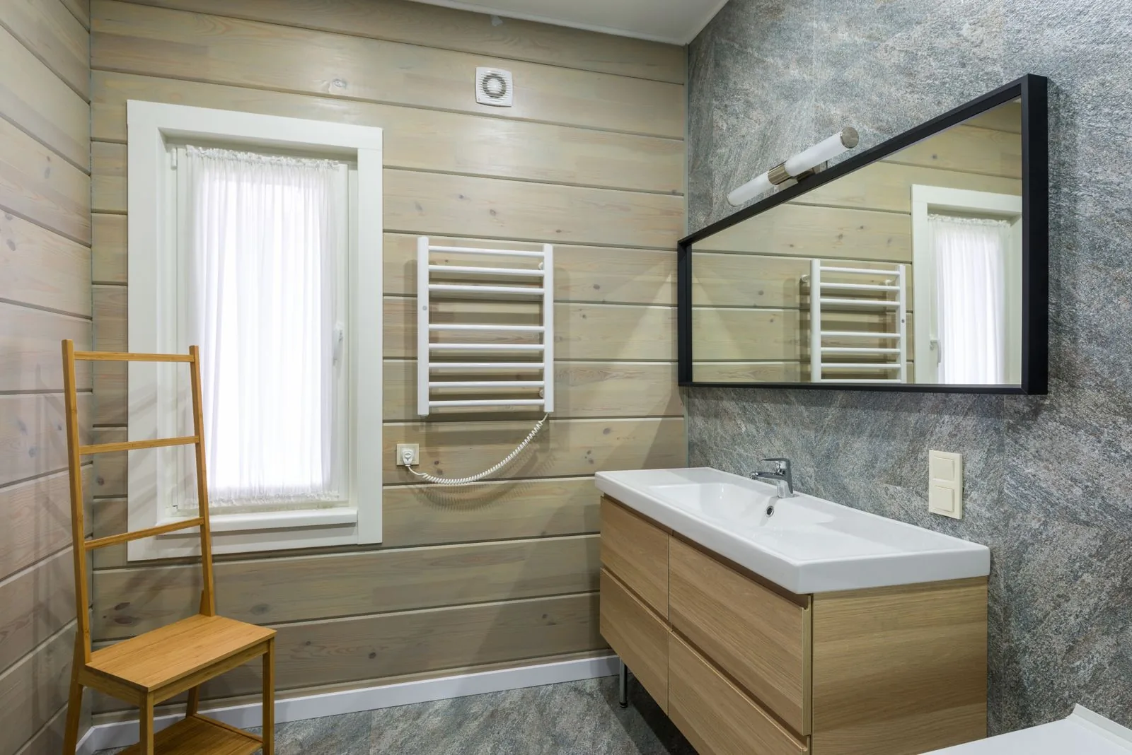 Wall-mounted heated towel rail with a towel next to a window in a light bathroom