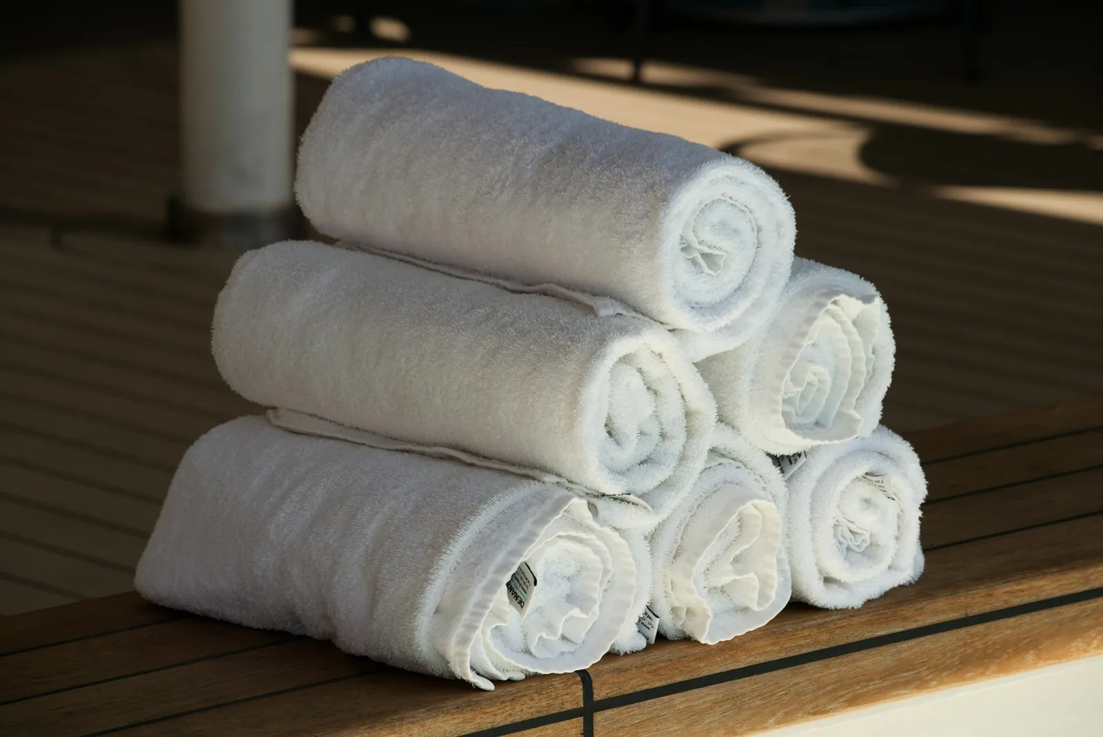 Stack of white rolled bath towels on a wooden deck, illustrating warm towels from an iHome towel warmer