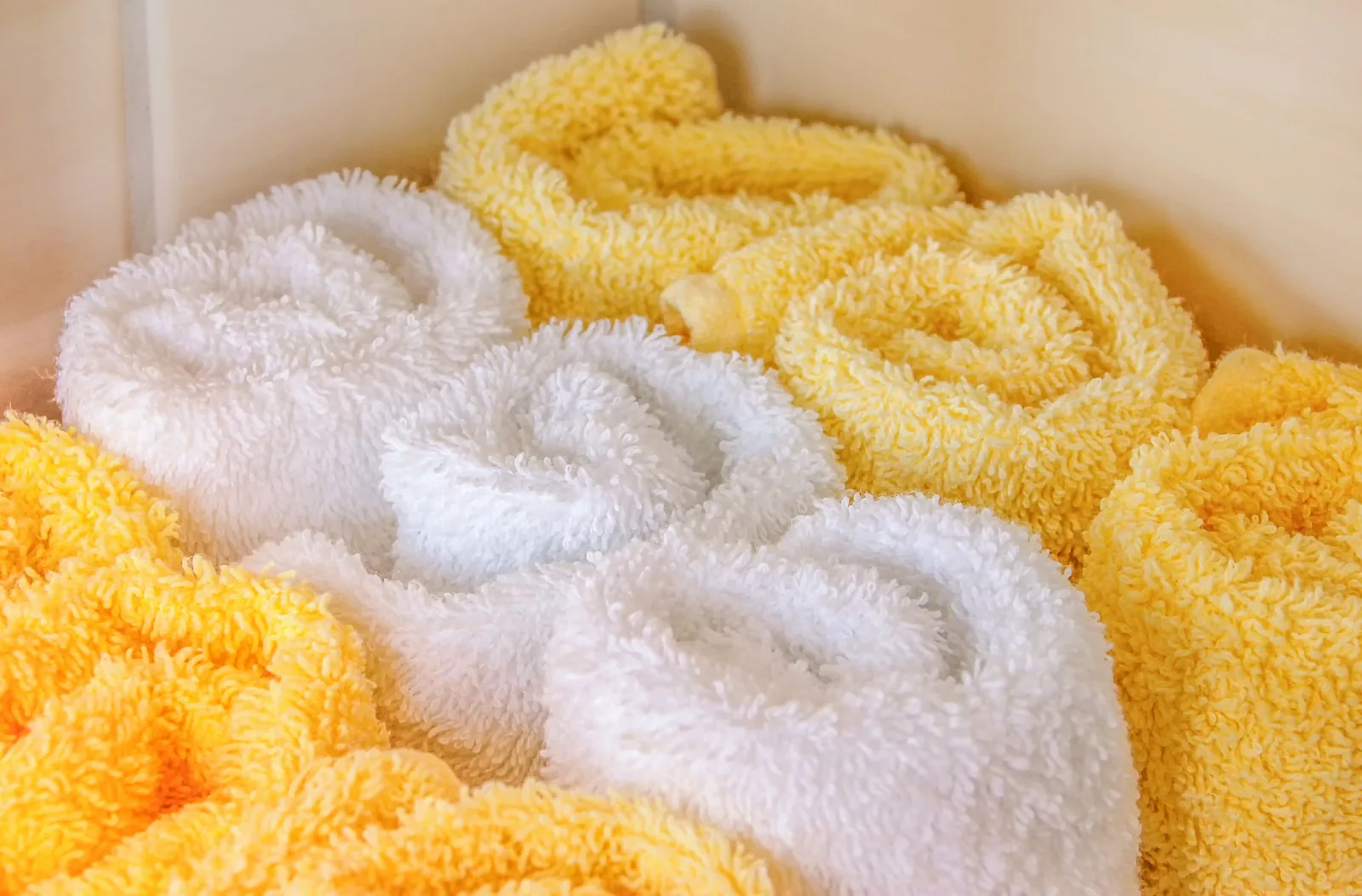 Rolled white and yellow bath towels stacked in a bathroom, ready for a bucket towel warmer